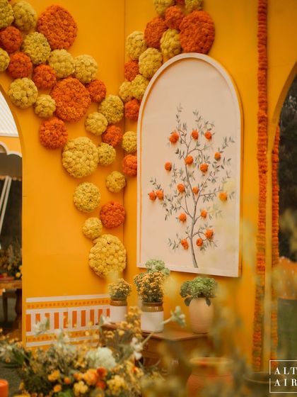 A hand-painted mural of an orange tree and a wall adorned with marigold pom-poms at the 'Kesar Sehar' Haldi. Every detail was designed to tell a story and invite inspiration.
