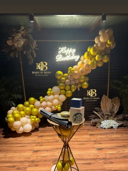 A sophisticated birthday setup with a diagonal balloon arrangement in gold and white. The decor is accented with pampas grass and a neon sign, creating a modern and elegant party vibe.