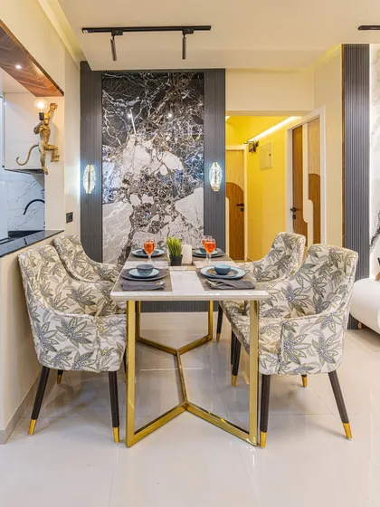 A closer look at the dining setup. The patterned chairs and gold-legged table add a touch of elegance, while the dark marble accent wall provides a bold, modern contrast.