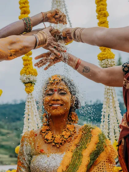 A bride enjoying a shower of rice and flowers during her Haldi. This shot captures a beautiful tradition and her serene expression, a moment of blessings and joy.