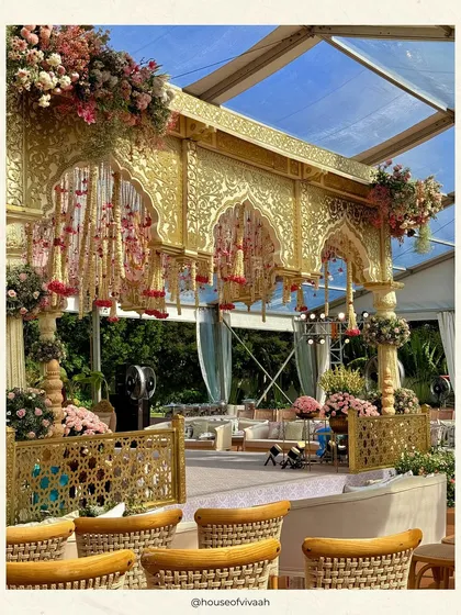A side view of the opulent gold and pink mandap, revealing the intricate jaali work and the clear-top tent that allows for an open-sky feeling while providing shelter.