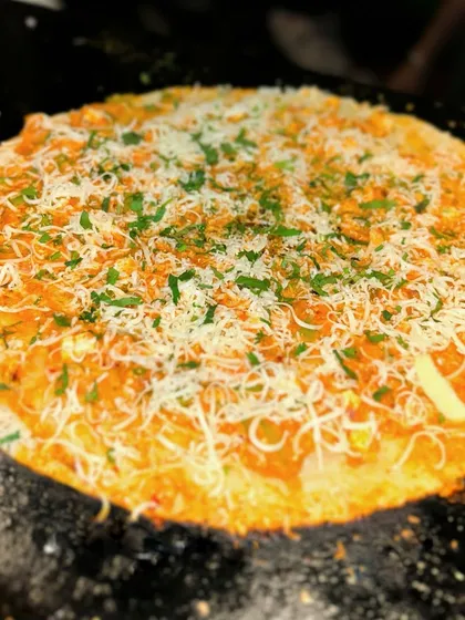 A close up of my Peri Peri Open Dosa on the hot griddle. The dosa is covered in a layer of spicy sauce and completely blanketed in melted cheese, making it a truly indulgent treat.
