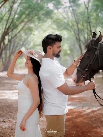 A stylish pose with a couple standing back-to-back, the groom stroking a horse while the bride adjusts her hat. This is a great example of a creative and posed shot within a nature theme.