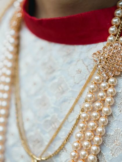 A close-up of the groom's sherwani, highlighting the elegant pearl necklace and brooch.