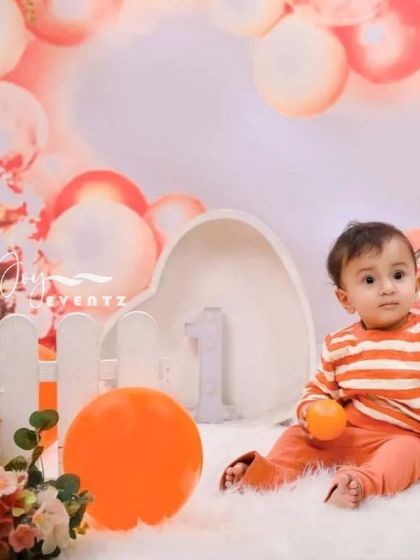 A warm and inviting tangerine-themed photoshoot. The baby boy, dressed in orange stripes, sits in a soft, fluffy setting with orange and white props, creating a bright and happy image.