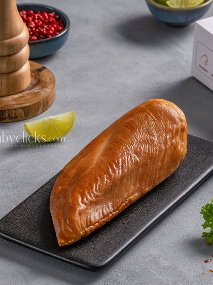 A smoked chicken breast from Zappfresh, simply styled on a black plate to highlight its golden-brown color.