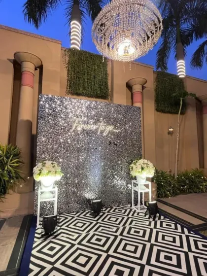 A modern and chic photo wall with a "Forever to go" neon sign against a silver sequin backdrop. The geometric floor adds a trendy touch to this reception setup.