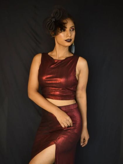 A full-length shot of the high-fashion look, featuring a metallic red outfit and a dramatic, artistic makeup style.