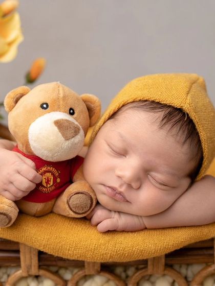 A sleepy newborn with his teddy bear. The yellow theme adds a cheerful touch to this cozy and cute portrait.