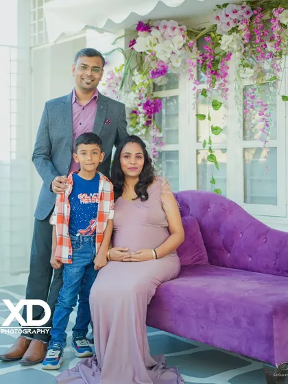 A formal family portrait with their son, taken in an elegant indoor studio with a purple chaise lounge.