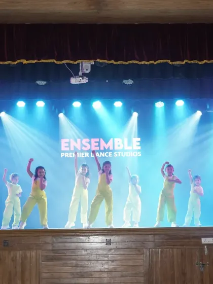 The full troupe on stage under the bright lights with our studio name proudly displayed behind them. This image captures the scale and professionalism of our student showcases.