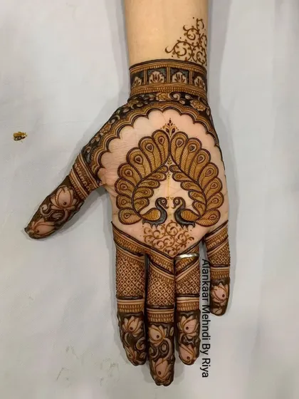 A beautiful design for the back of the hand, with two peacocks forming a heart shape with their necks, perfect for an engagement or sangeet.