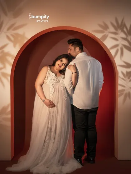 A tender moment between the couple within the red arch. The dad-to-be's gentle kiss on her head is a perfect expression of love and care.
