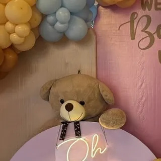 A large teddy bear looks over a neon 'Oh Baby' sign, creating a sweet and modern photo opportunity.