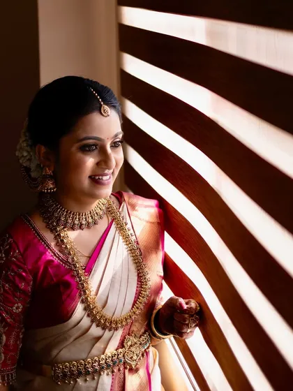 A beautiful portrait of a bride by the window. The natural light highlights the flawless, dewy finish of her makeup and the intricate details of her temple jewelry.