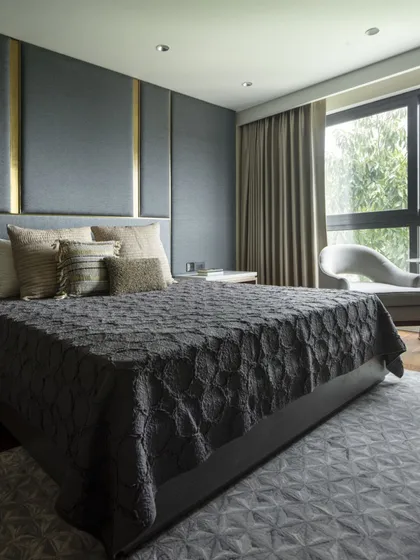 A bedroom featuring a dramatic, floor-to-ceiling upholstered headboard with brass inlay. The dark, moody color palette and geometric-patterned rug create a sophisticated and luxurious feel.