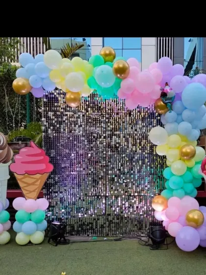 An ice cream themed party setup with a silver sequin backdrop. The pastel balloon arch is complemented by large ice cream cone props.