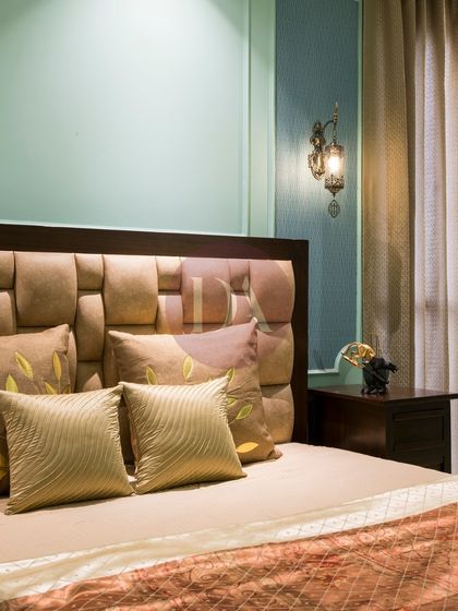 This bedroom features a unique, cushioned headboard and a soft, mint-green accent wall. The vintage-style wall sconces add a touch of classic charm, creating a cozy and inviting atmosphere.