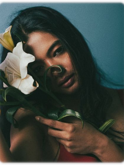 A gentle and intimate portrait where the model embraces the flowers. Her expression is serene, and the lighting creates a soft glow on her skin. This shot feels personal and emotional, perfect for a fine art beauty series.