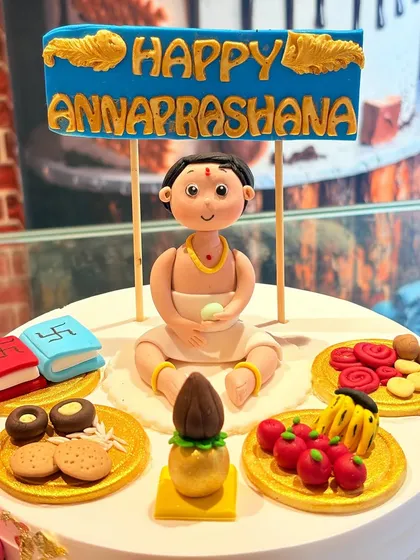 A close-up of a detailed Annaprashan ceremony cake topper, featuring a baby's first rice-eating ceremony with traditional elements.