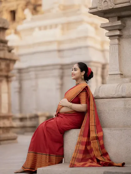 Seated on the temple steps, this mother-to-be looks radiant in her red saree, capturing a moment of quiet joy and anticipation.