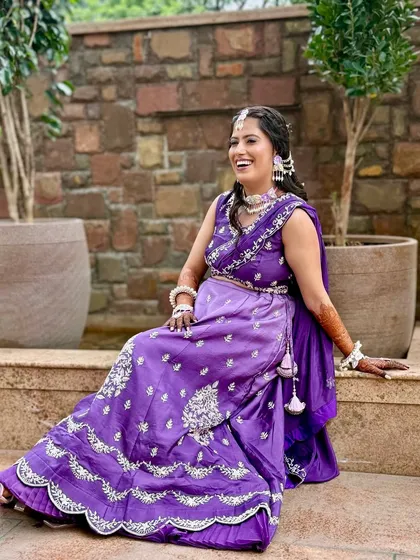 A full-length shot of the bride, looking happy and relaxed. The unconventional purple outfit is perfectly complemented by the soft, glowing makeup.