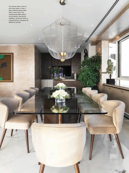 A magazine feature of a dining area we designed, highlighting the elegant glass-topped table and plush velvet chairs. The ethereal pendant light from Moooi adds a sense of lightness and sophistication, creating a perfect setting for a luxurious meal.