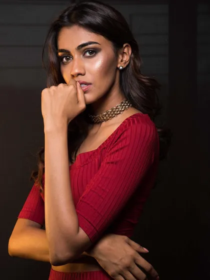 A close-up portrait of Apeksha in the red outfit. The choker neckline and ribbed fabric create a sleek and sophisticated silhouette.