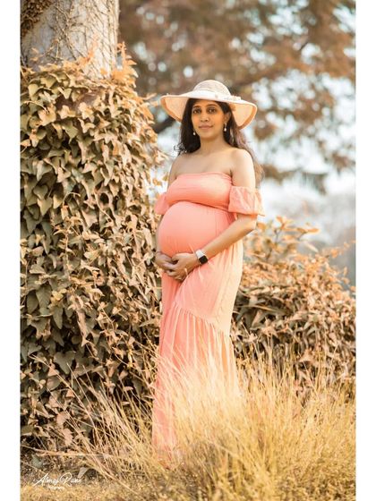 This portrait showcases how simple props, like a sun hat, can add style and personality to a solo maternity shoot. The mother-to-be looks elegant in a peach off-shoulder gown.