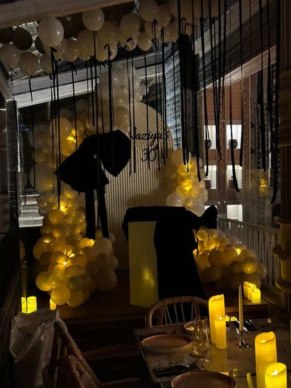 A moody, candlelit view of Naziya's bow-themed 30th birthday party. The combination of warm lights, white balloons, and black ribbon streamers created a sophisticated and intimate atmosphere.