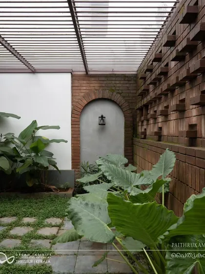 A private courtyard features a distinctive brick wall with protruding blocks, creating a textural backdrop for the lush tropical plants.