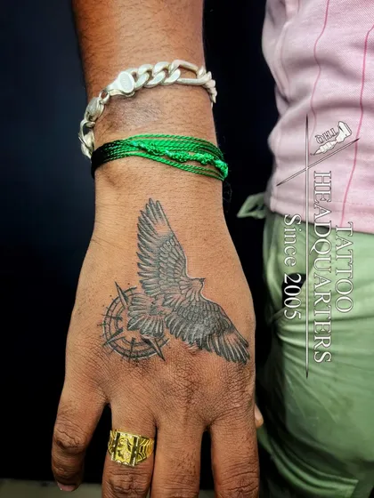 A tattoo of a bird with a compass on the hand, symbolizing finding your way and freedom.