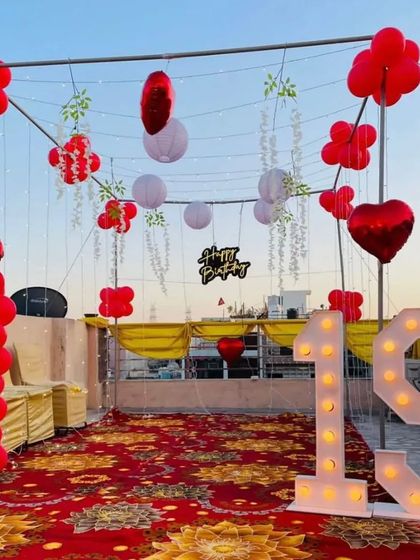 A 19th birthday celebration on a rooftop, featuring red balloon pillars, hanging lanterns, and large light-up marquee numbers.