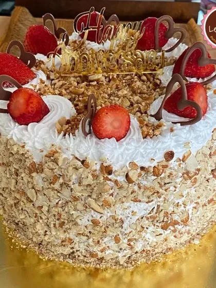 A beautiful strawberry and almond cake. The sides are coated in crunchy toasted almonds, and the top is adorned with fresh strawberries and delicate chocolate hearts.