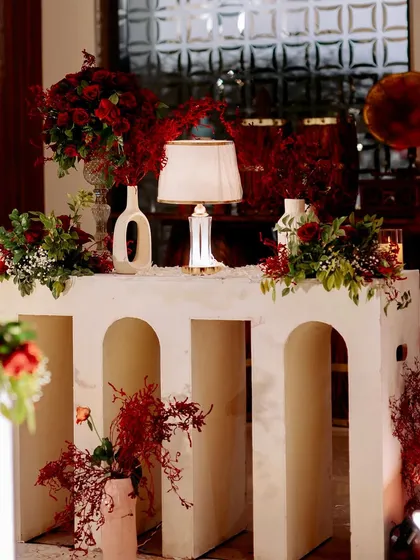 A close-up of the decor details, including the modern console table, minimalist vases, and a classic table lamp, all surrounded by rich red florals.