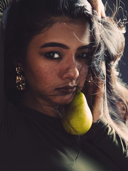 Introducing a simple prop like a pear can add an unexpected, artistic element to an editorial. It creates a point of interest and a touch of surrealism. The lighting remains focused on the model's expression and the rich, earthy tones of the shot.