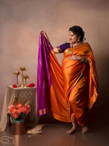 The way she holds the pallu of her saree shows its beautiful color and texture, adding a dynamic element to the portrait.