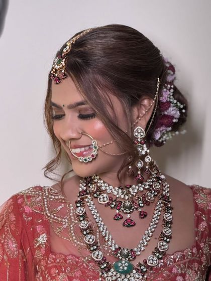 A smiling bride wearing a heavy, multi-colored stone necklace set. The floral arrangement in her hair adds a fresh, beautiful touch to the overall look.