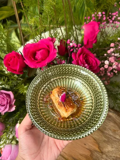 A cube of sesame-crusted paneer in a sweet and spicy sauce, beautifully plated in a green glass bowl.
