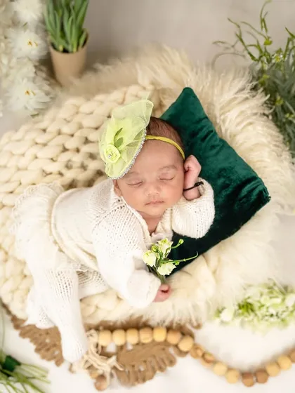 Freshly picked from heaven’s garden. This overhead shot captures a baby in a white knit outfit, surrounded by an abundance of fresh white flowers and greenery.