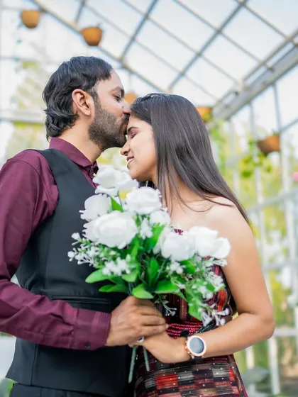 A tender moment where the groom kisses the bride's forehead in a beautiful glasshouse set, surrounded by greenery.