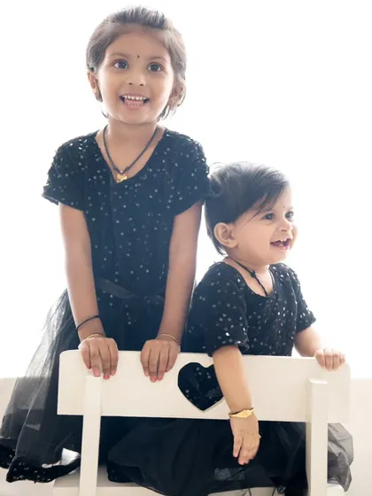 Two sisters in matching black dresses share a happy moment. The simple white bench and background make their joyful expressions the star of the photo.