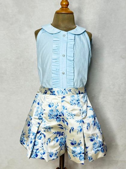 The front view of our "Happy Blues" shorts set. The sleeveless collared shirt has delicate pintucks, pairing beautifully with the pleated floral shorts.