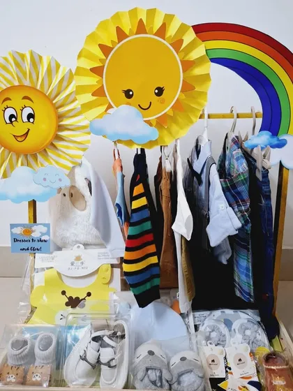 A beautiful 'Sunshine and Rainbow' themed clothing display for a baby boy. This Jamna packing arrangement includes a variety of outfits, from casual striped shirts to formal wear, along with tiny shoes and socks.