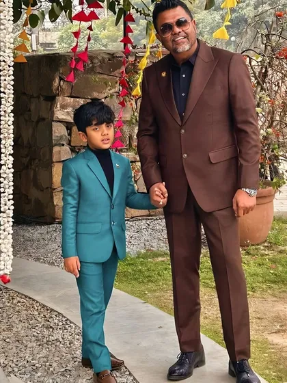 A father and son duo in custom Levelline suits. The son's vibrant teal suit is a fantastic choice for a festive outdoor event, while the father's brown suit is classic and versatile.