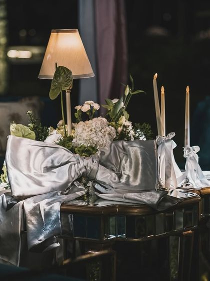 A table centerpiece with a lamp and a large silver bow, seen at night.