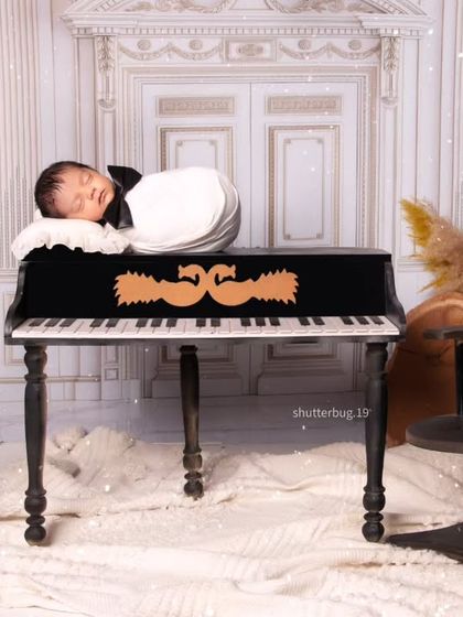 A classic newborn pose, with the baby sleeping on top of the miniature grand piano. The composition is balanced with elegant candlesticks and pampas grass arrangements.
