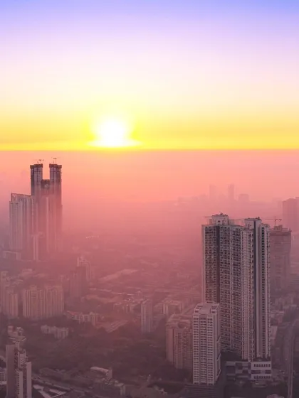 The sun appears as a bright orb in a hazy pink sky, setting behind the tall buildings of Mumbai.