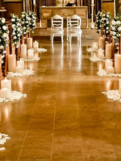 A simple and serene setup for a Christian wedding ceremony. The aisle is lined with candles and white rose petals, leading to two elegant chairs at the altar.