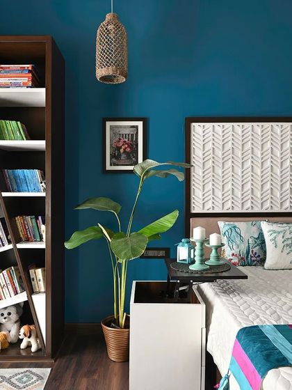A bold teal accent wall serves as the vibrant backdrop for this bedroom. The headboard features a custom panel with a CNC-cut geometric pattern, and a large plant adds a touch of nature, creating a fresh and energetic space.